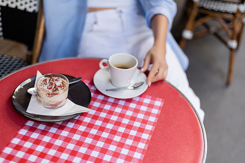 Cropped view of tiramisu and coffee near blurred woman on cafe terrace in France