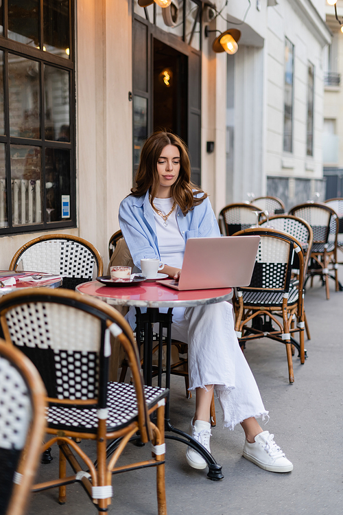 Young freelancer using laptop near dessert and coffee on cafe terrace in Paris