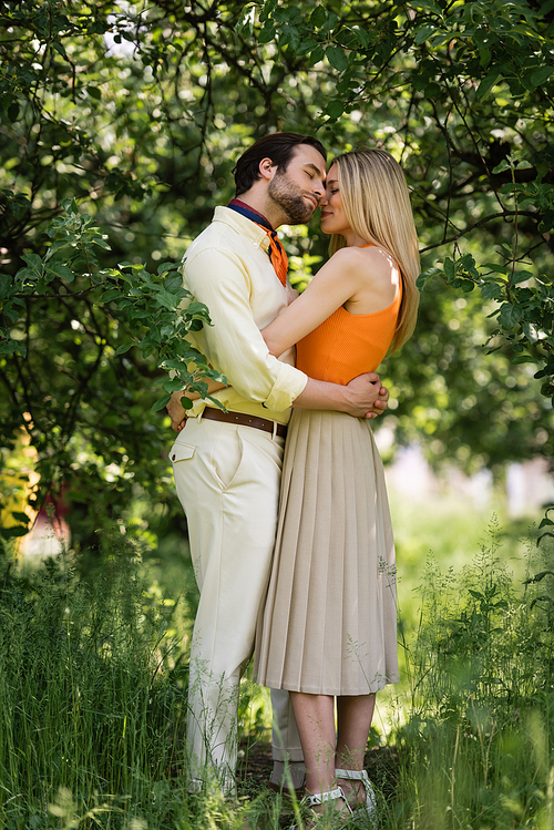 Side view of stylish couple embracing near trees in summer park