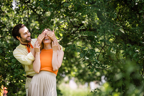 Stylish man covering eyes to cheerful girlfriend in summer park