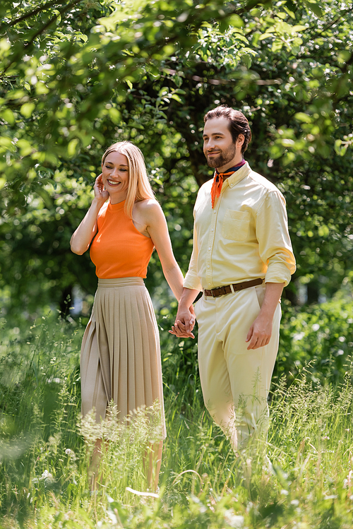 Positive stylish couple walking in summer park