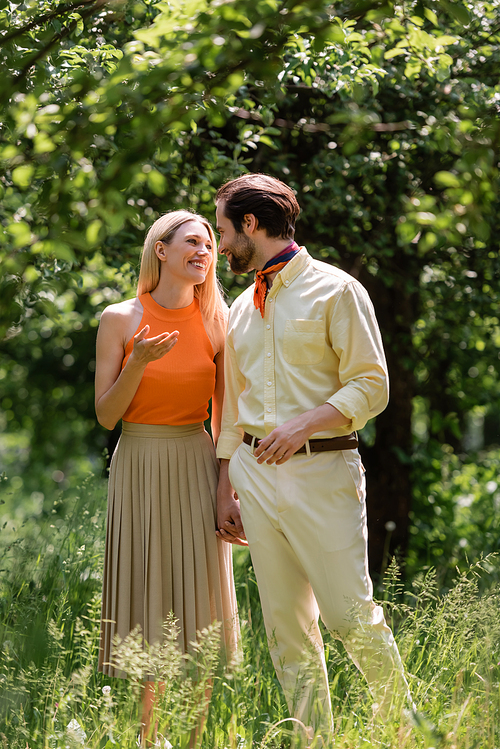 Smiling woman talking to stylish boyfriend while walking in summer park