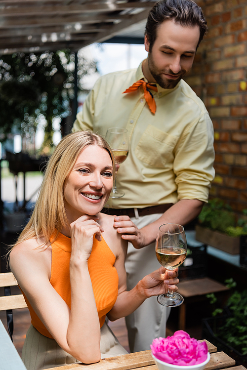 Smiling woman holding glass of wine near stylish boyfriend in outdoor cafe