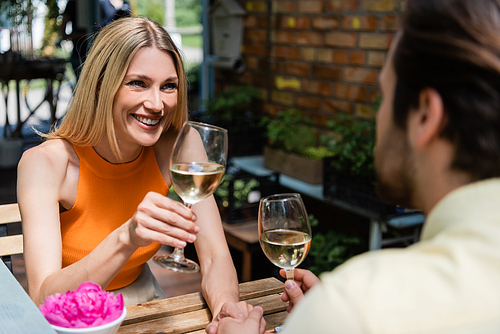 Happy woman holding glass of wine near blurred boyfriend in outdoor cafe