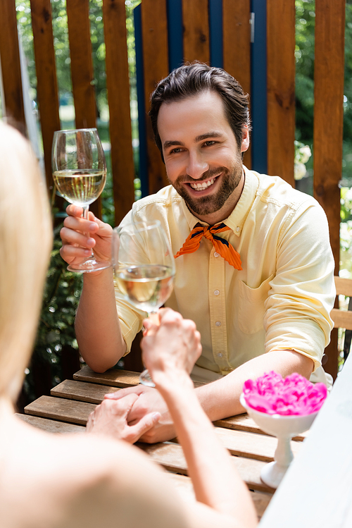 Stylish man holding glass of wine and hand of girlfriend in outdoor cafe