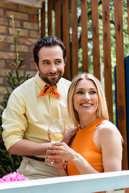 Smiling woman holding glass of wine near trendy boyfriend in outdoor cafe