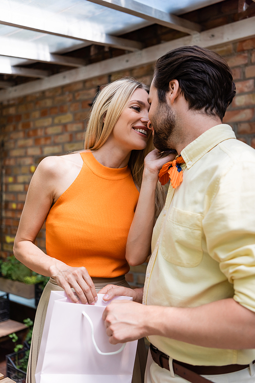 Cheerful woman kissing boyfriend with shopping bag in outdoor cafe