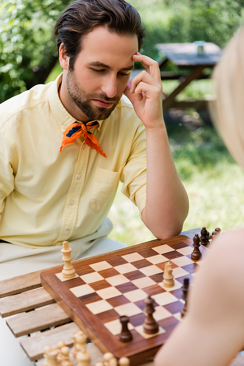 Pensive man playing chess with blurred girlfriend in park