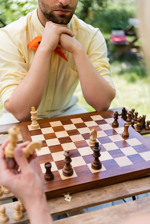 Cropped view of man sitting near blurred girlfriend holding chess in park
