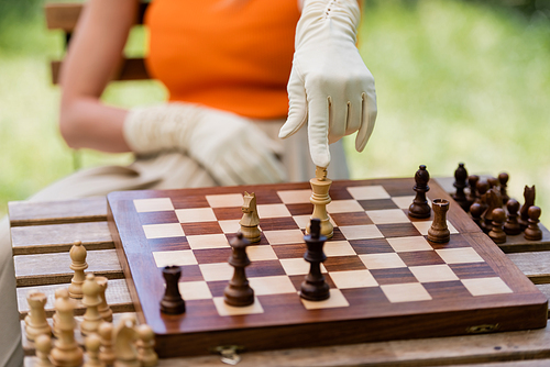 Cropped view of stylish woman pointing at chess figure on board in park