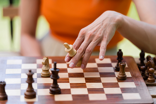 Cropped view of woman holding chess figure near board in park
