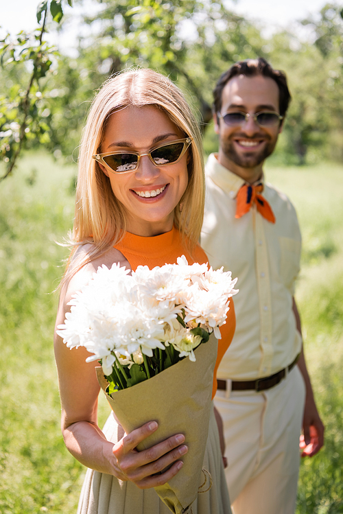 Fashionable woman looking at chrysanthemums near blurred boyfriend in park