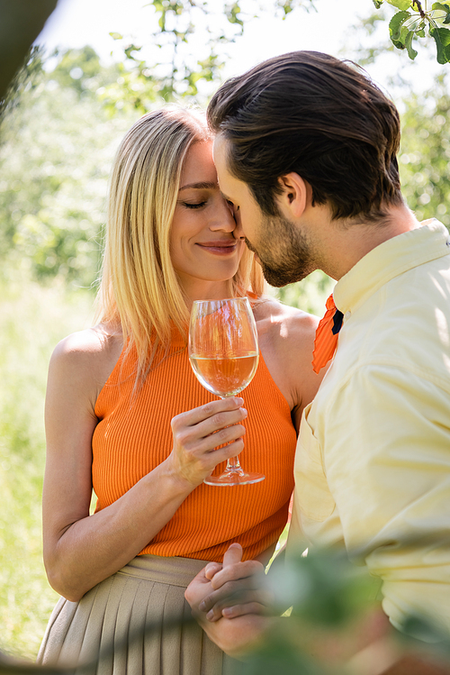 Smiling woman holding glass of wine and hand of stylish boyfriend in summer park