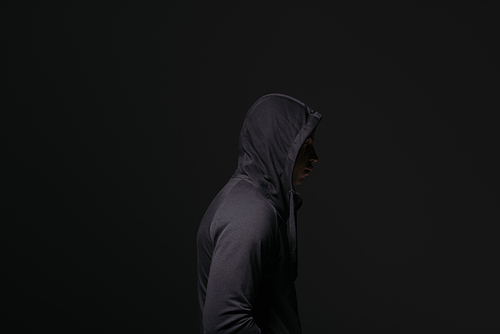 Side view of african american hooligan in hood standing isolated on black