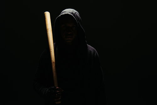 Silhouette of hooligan in hoodie holding baseball bat isolated on black with lighting