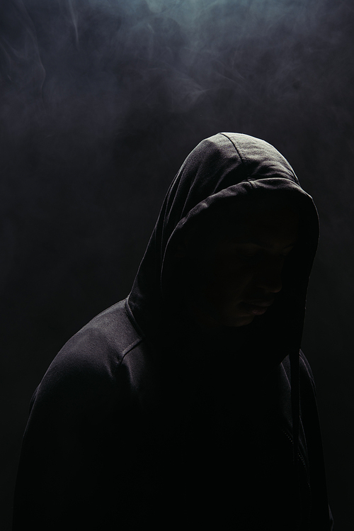 Silhouette of bandit in hoodie on black background with smoke