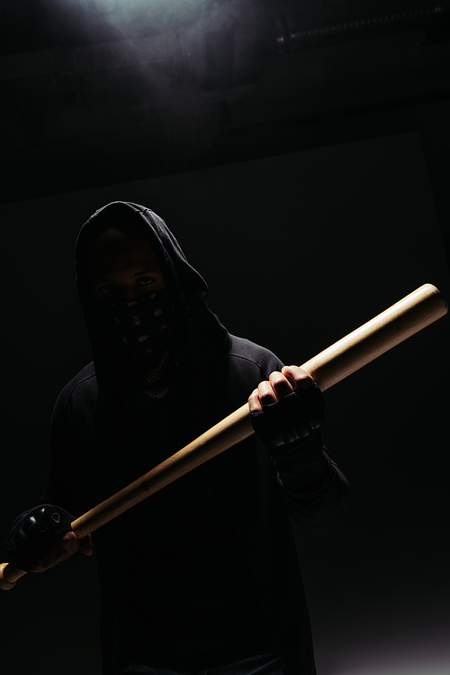 Silhouette of african american vandal holding wooden baseball bat on black background with smoke