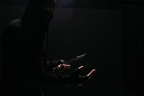 Side view of african american bandit in mask holding knife isolated on black