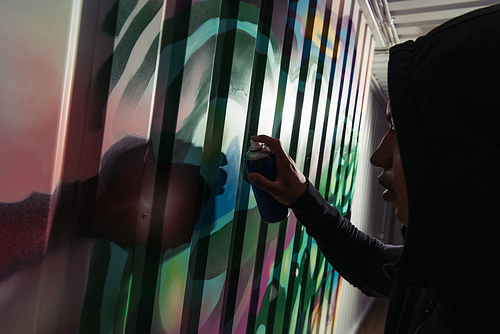 Side view of african american vandal drawing graffiti on wall