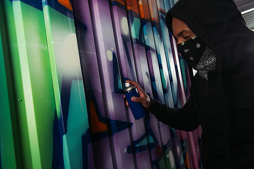 Side view of african american vandal with mask on face drawing graffiti on wall