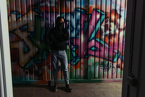 African american vandal with mask on face standing near graffiti on wall