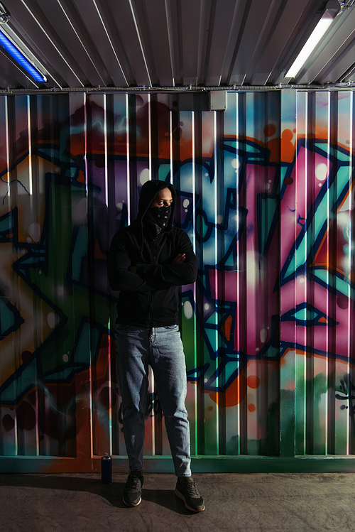 African american vandal in hoodie standing near spray paint and graffiti on wall