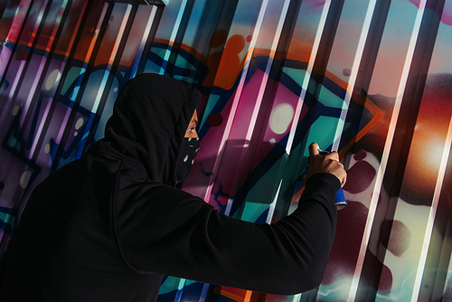 Side view of african american vandal drawing graffiti on wall outdoors at night