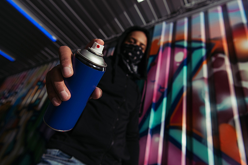 Low angle view of blurred african american vandal holding spray paint near graffiti on wall