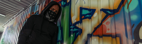 Low angle view of african american vandal looking at camera near graffiti on wall, banner