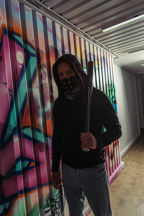 African american vandal holding baseball bat near graffiti on wall