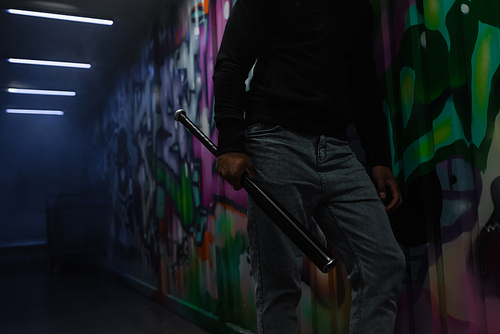 Cropped view of african american bandit holding baseball bat near graffiti on wall in garage