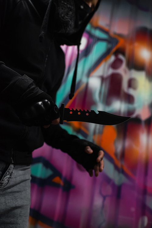 Cropped view of african american robber holding knife near blurred graffiti on wall outdoors