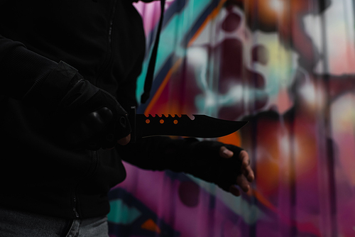 Cropped view of african american robber holding knife near graffiti on urban street