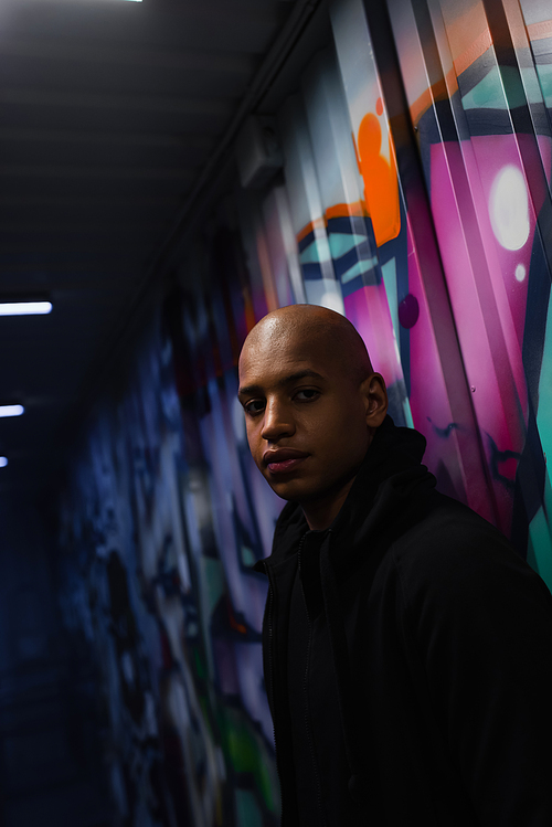 African american hooligan looking at camera near graffiti in garage