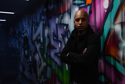 African american hooligan looking at camera near graffiti in garage