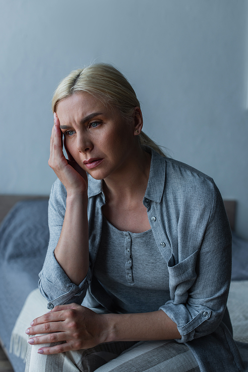 exhausted blonde woman with menopause suffering from headache in bedroom
