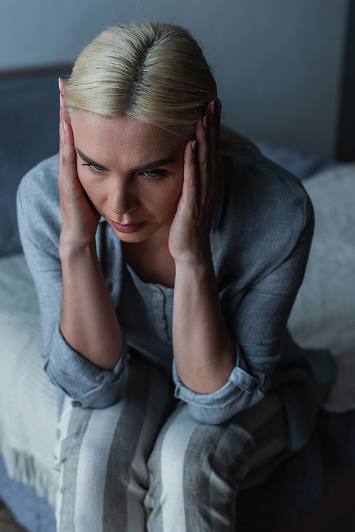 high angle view of exhausted blonde woman with menopause suffering from headache in bedroom