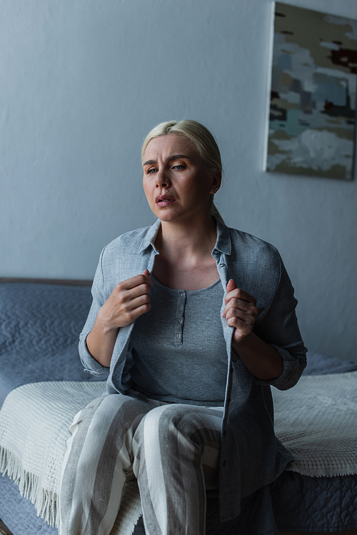 blonde woman with menopause suffering from heat and touching cardigan in bedroom