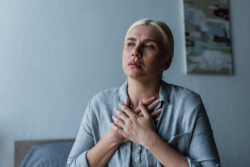 blonde woman with menopause touching chest while suffering from heat in bedroom