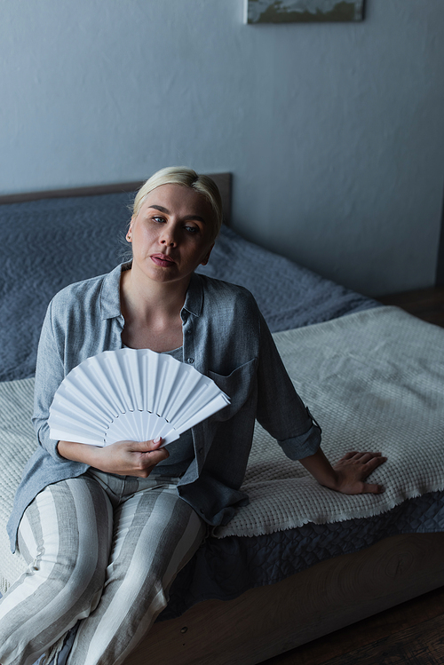 blonde woman with menopause suffering from heat and cooling with fan in bedroom