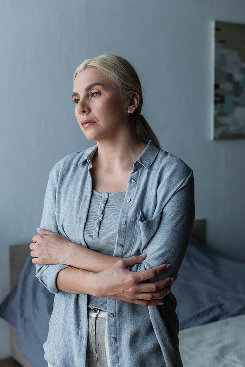 depressed woman with menopause standing with crossed arms and looking away
