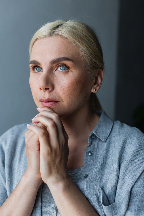 portrait of blonde woman with blue eyes and clenched hands praying at home