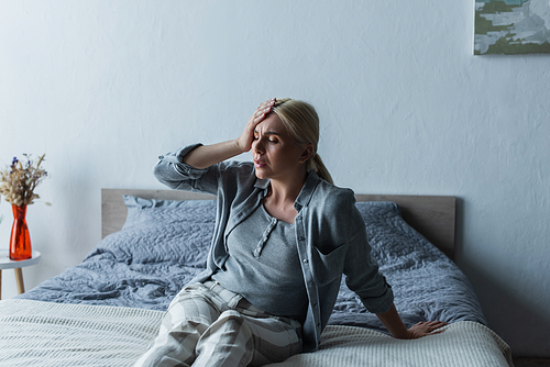 upset blonde woman with menopause suffering from migraine in bedroom