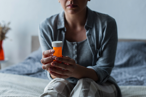 cropped view of woman with menopause holding bottle with pills and sitting on bed