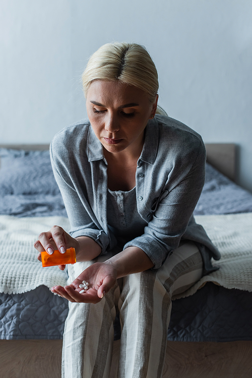 upset blonde woman with menopause holding bottle and pouring pills in hand