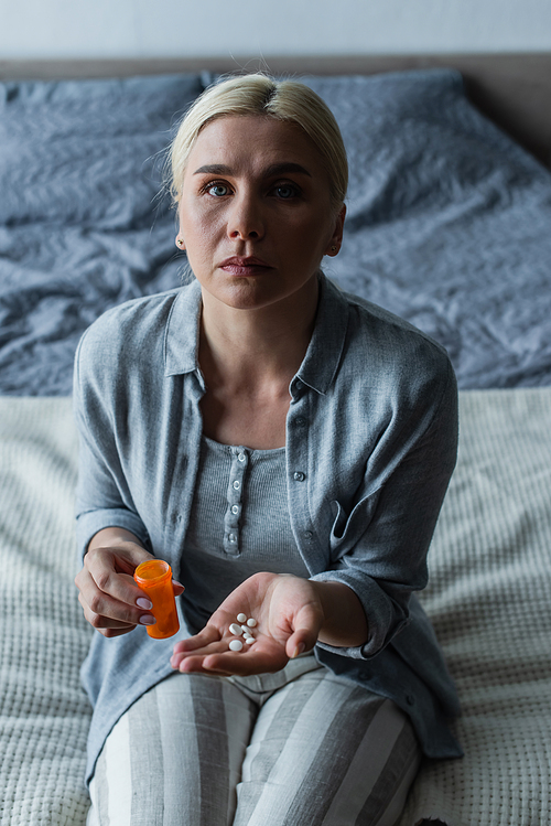 upset blonde woman with menopause holding bottle and pills in hands