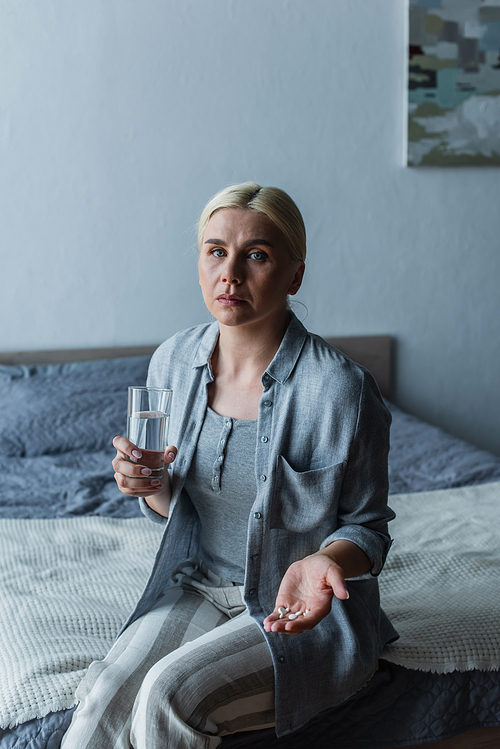 woman with menopause holding pills and glass of water while sitting on bed