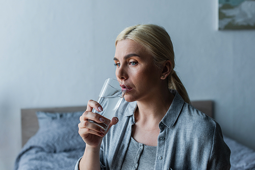 pensive woman with menopause drinking fresh water from glass