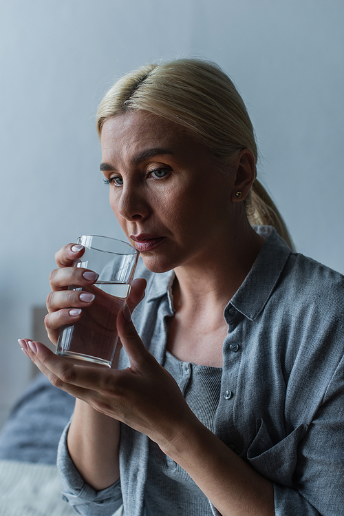 sad blonde woman with menopause drinking fresh water from glass