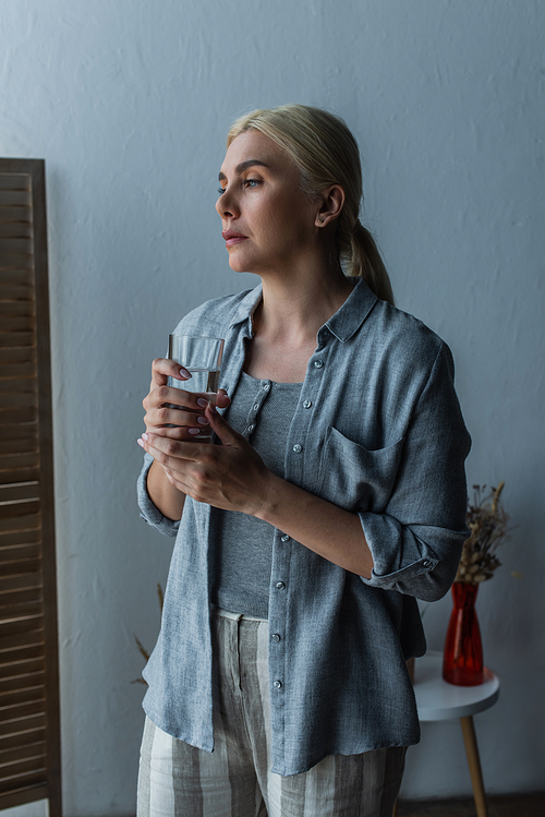 blonde woman with menopause holding glass of water and looking away